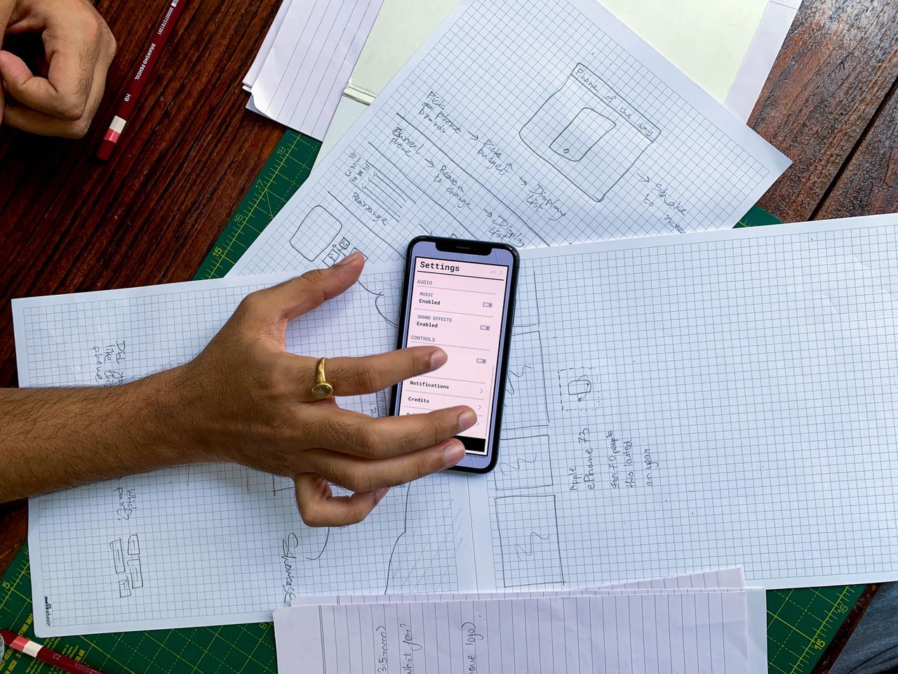 services-02 Hand holding smartphone over app design sketches on papers, top view.